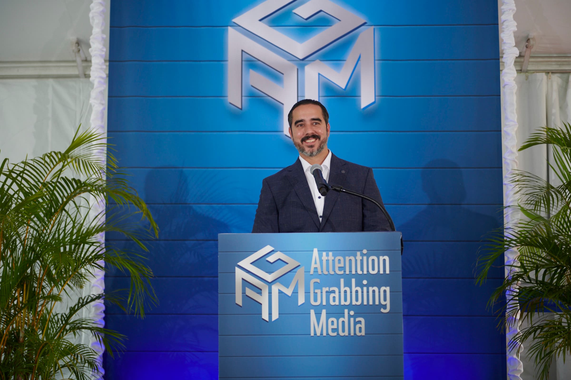 Manuel Suarez smiling at a branded podium under the AGM logo backdrop