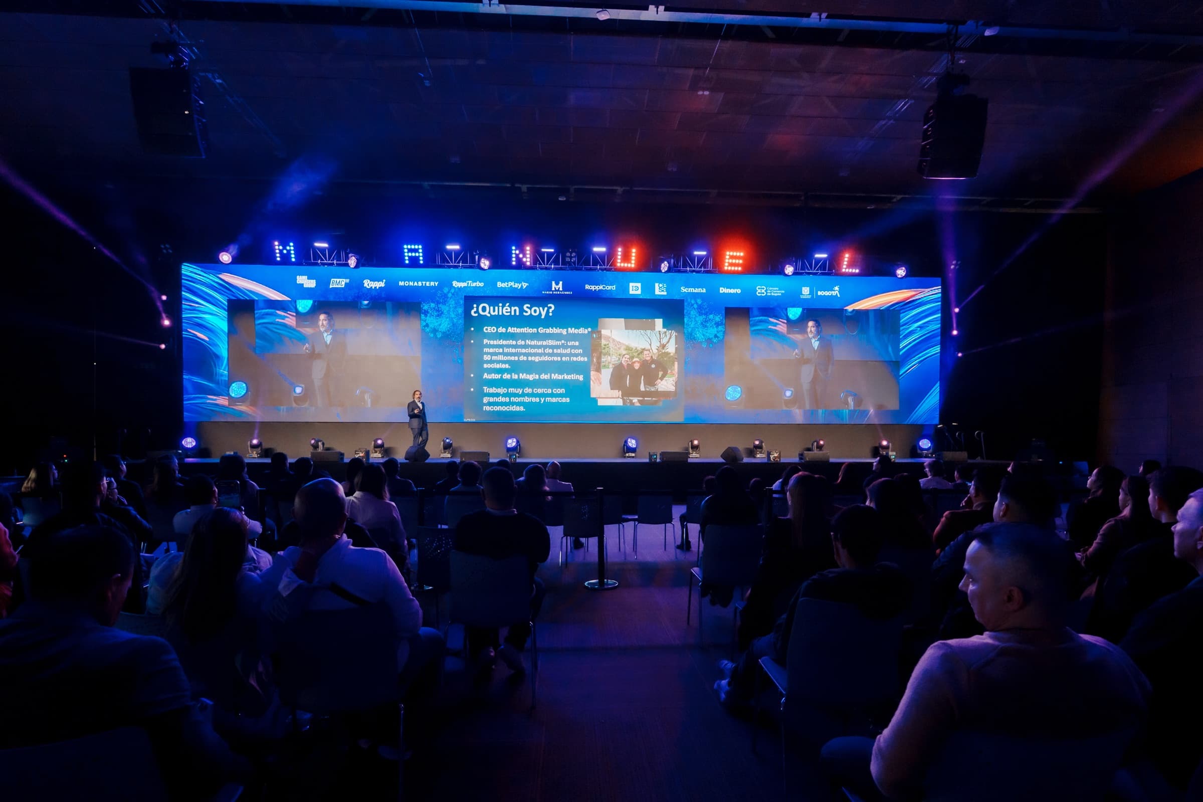 Manuel Suarez on stage delivering a keynote to a packed house, his name in lights above the screen