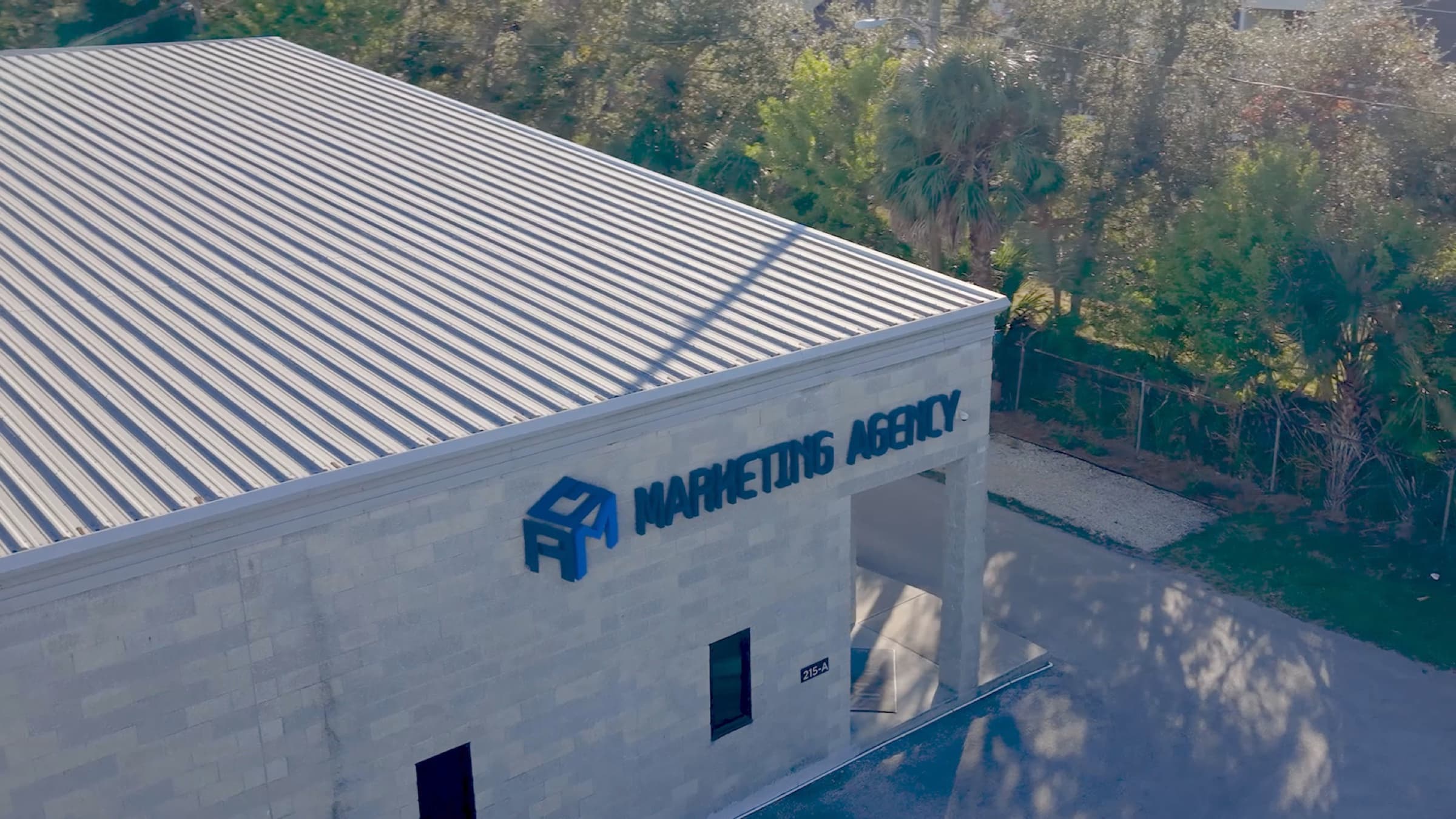 High drone angle over the AGM building rooftop and sign, greenery behind