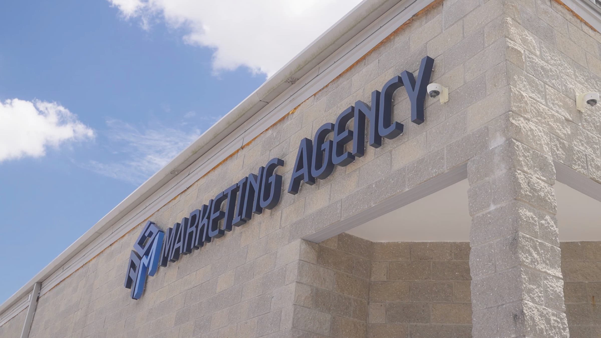 Low-angle close-up of the AGM Marketing Agency sign against a blue sky