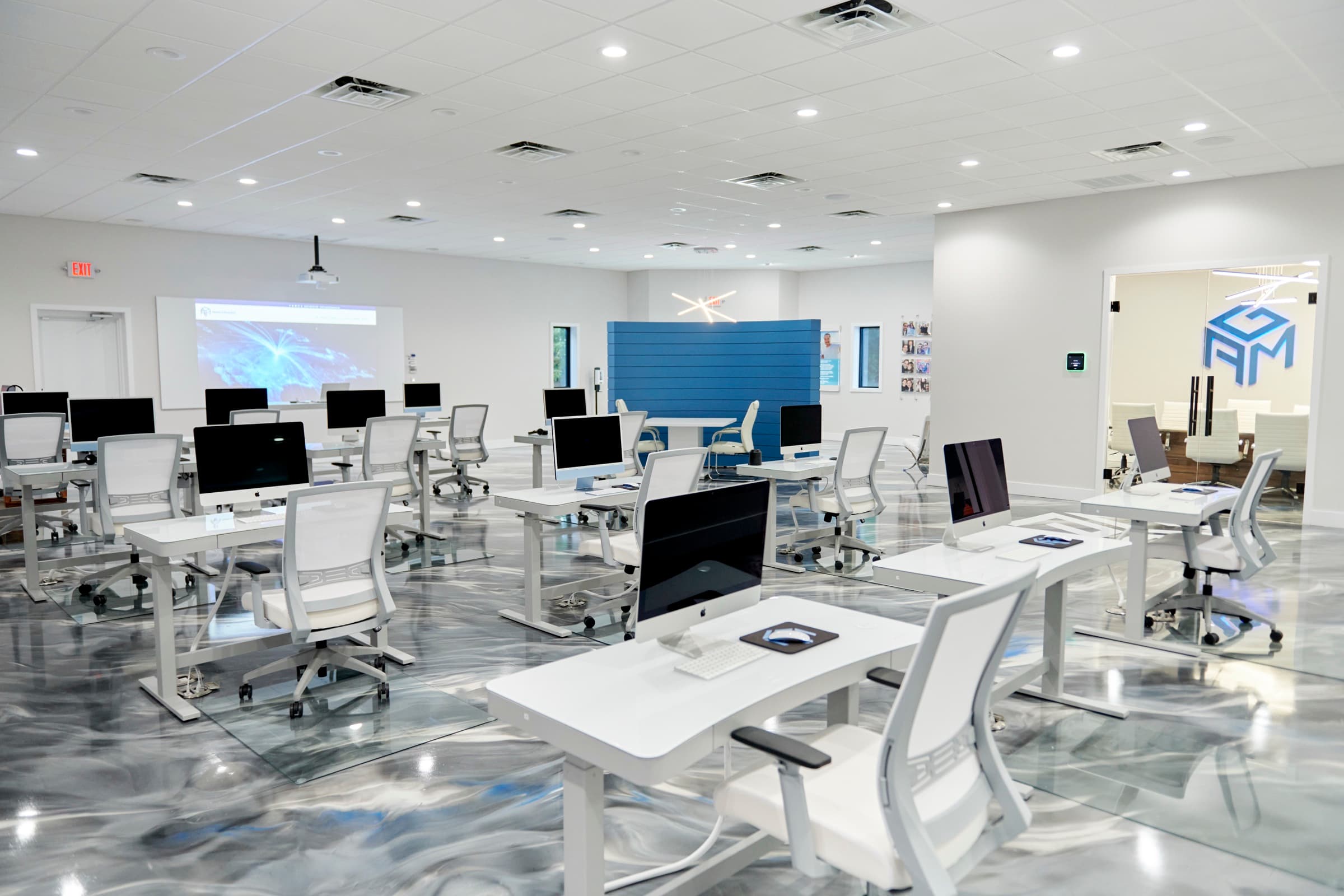 Open office floor with rows of white standing desks and iMacs