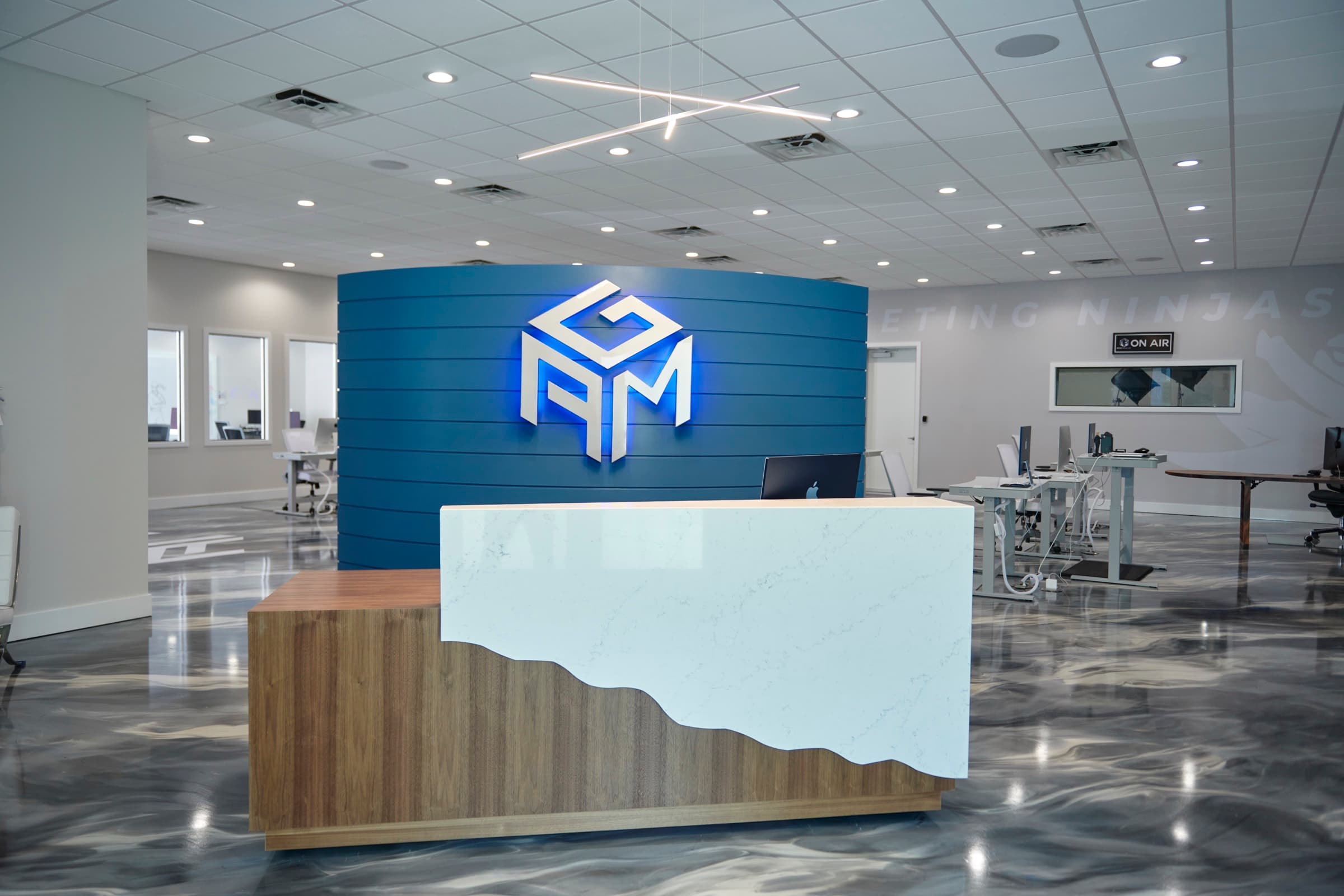 AGM reception: backlit cube-logo wall in navy behind a marble-and-walnut desk on a marbled epoxy floor